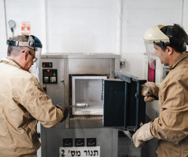 Two researchers in a laboratory wear protective clothing as they insert an object into a device.