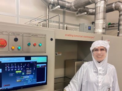 A female researcher in a laboratory wearing a sterile white coat and goggles and smiling